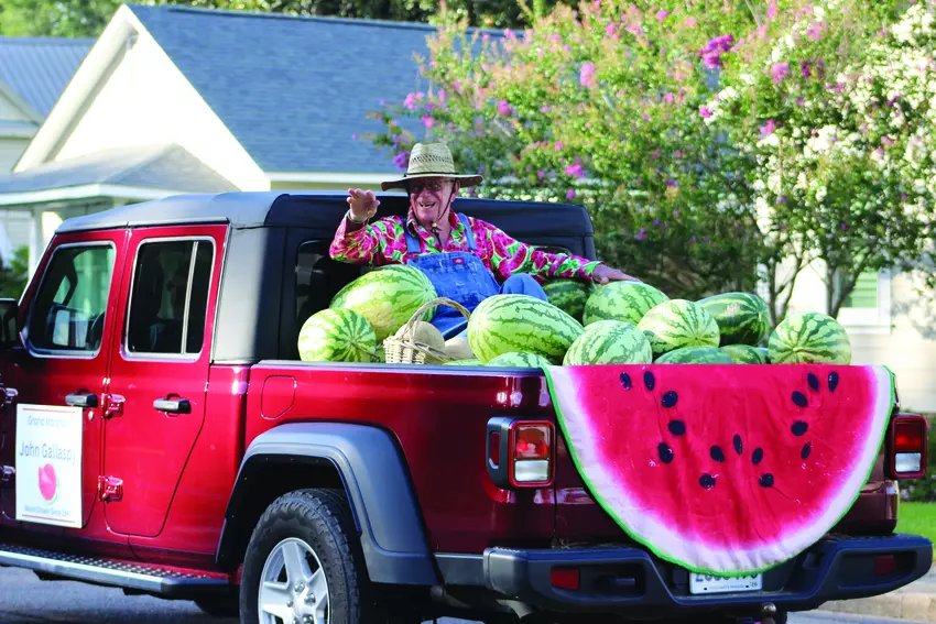 A parade grand marshal waves from a red pickup filled with watermelons at the Washington Parish Watermelon Festival.